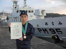 「あまみ」の前で賞状を示す芦刈通信士補